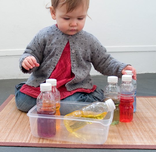 Bébé joue avec bouteilles colorées Montessori